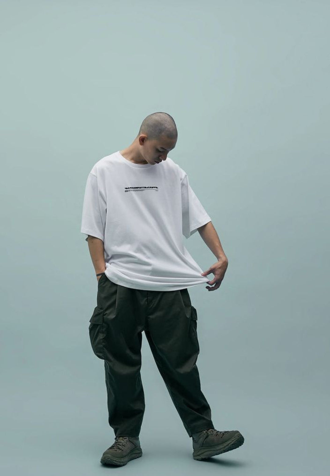 Person wearing a white t-shirt and dark pants on a light gray background